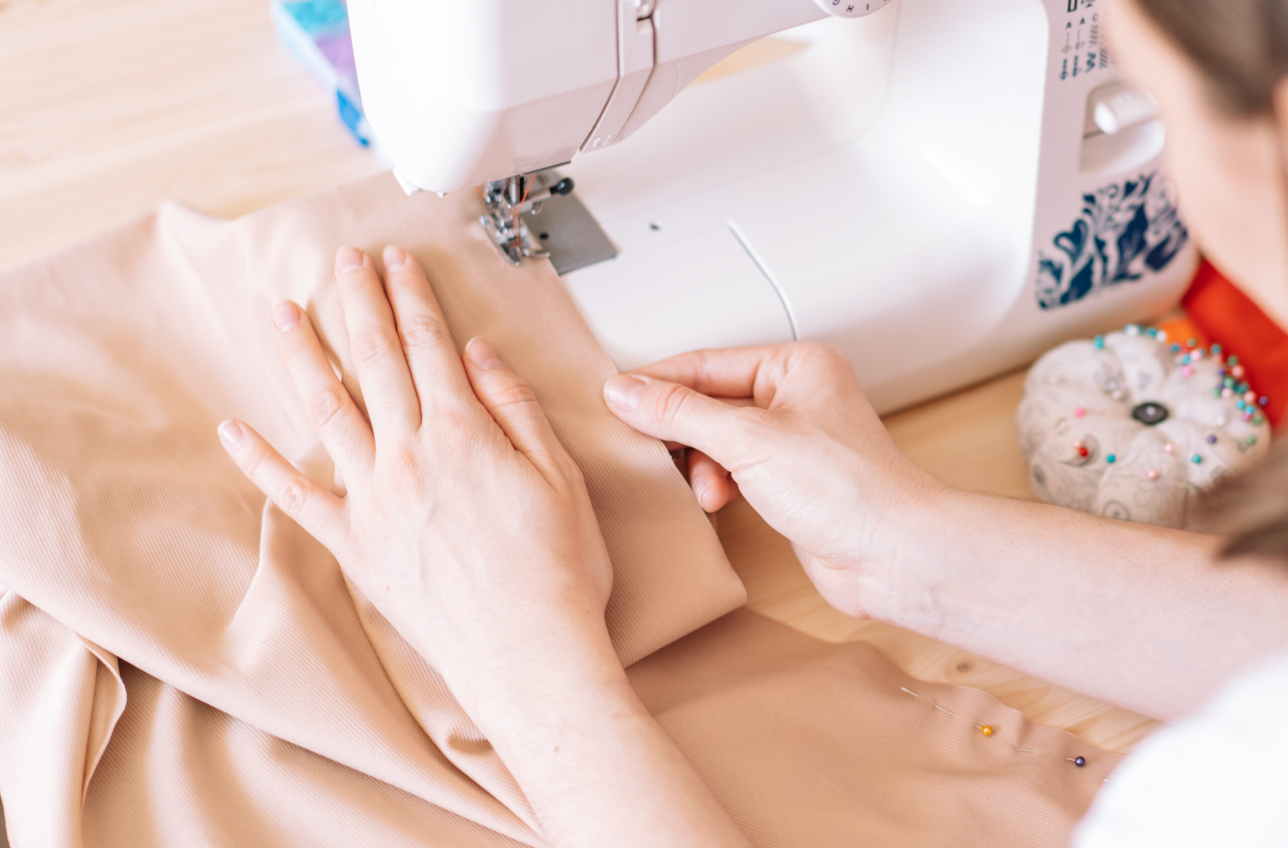 Lady sews on a sewing machine on a wooden table.
